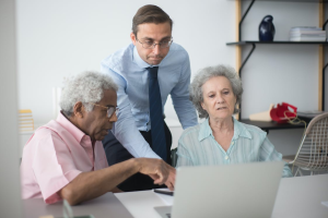 a man standing between elderly people sitting at a desk.