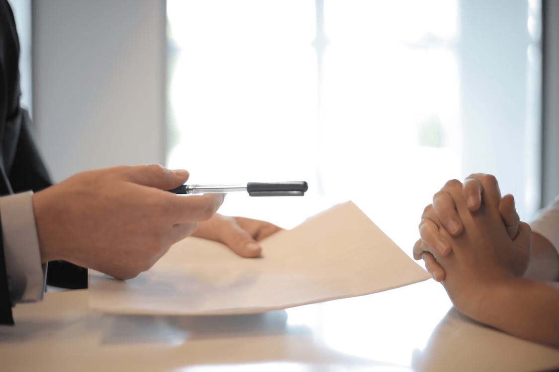 a person handing over a pen and paper.