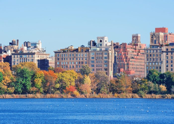 Central Park Autumn with New York City Manhattan Midtown skyline skyscrapers over lake with colorful foliage and clear blue sky.