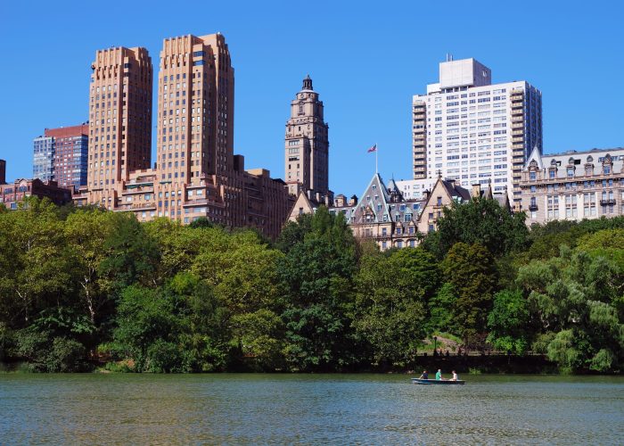 New York City Central Park with Manhattan skyline skyscrapers and blue sky with boat in lake.