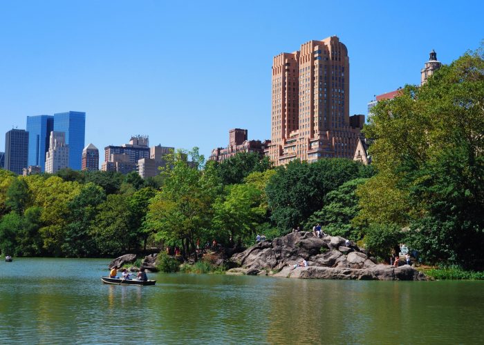New York City Central Park with Manhattan skyline skyscrapers and blue sky with boat in lake.